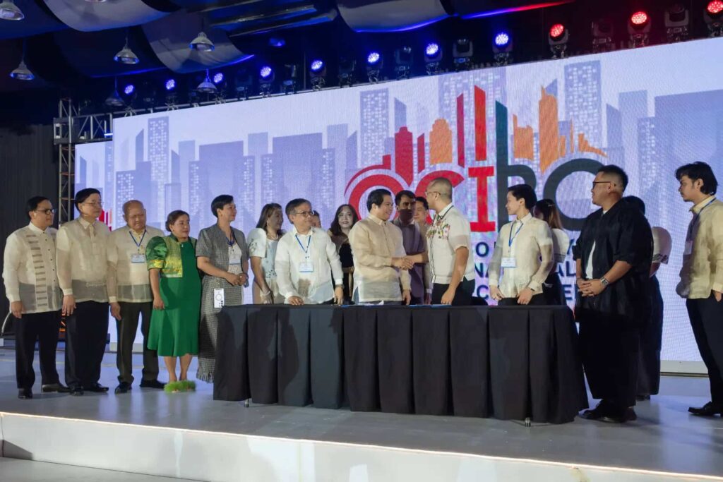 A line of people in formal attire shaking hands on a stage at an events and experiences summit.