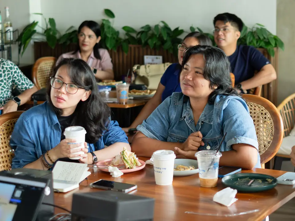 Group of people sitting around a cafe table, listening attentively during a membership meetup.