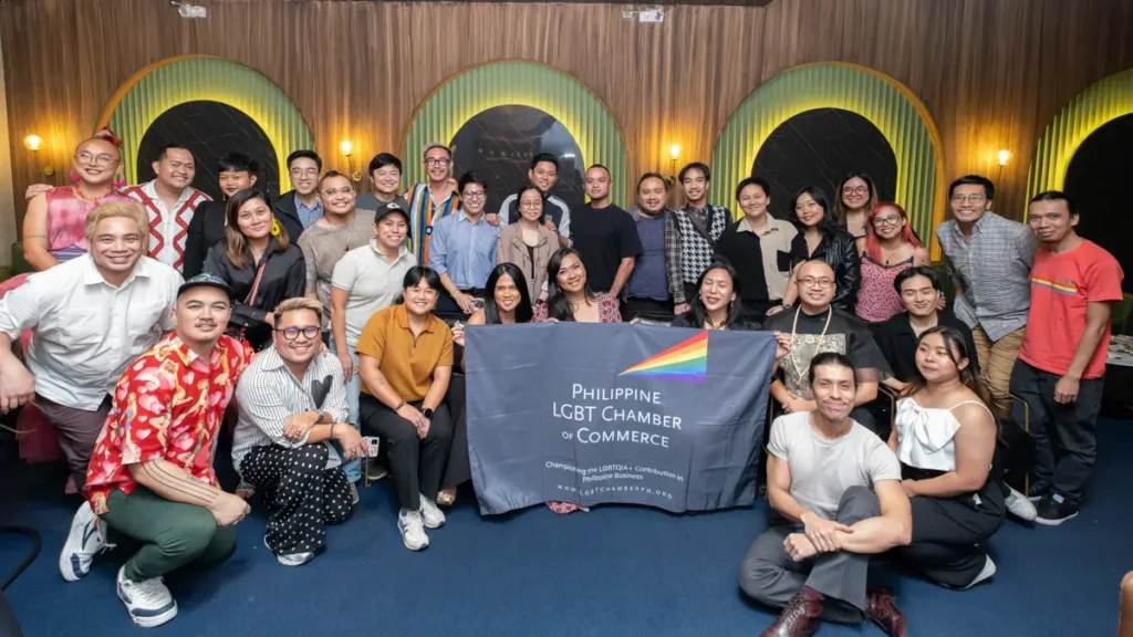A large group of people smiling and posing together behind a Philippine LGBT Chamber of Commerce banner.
