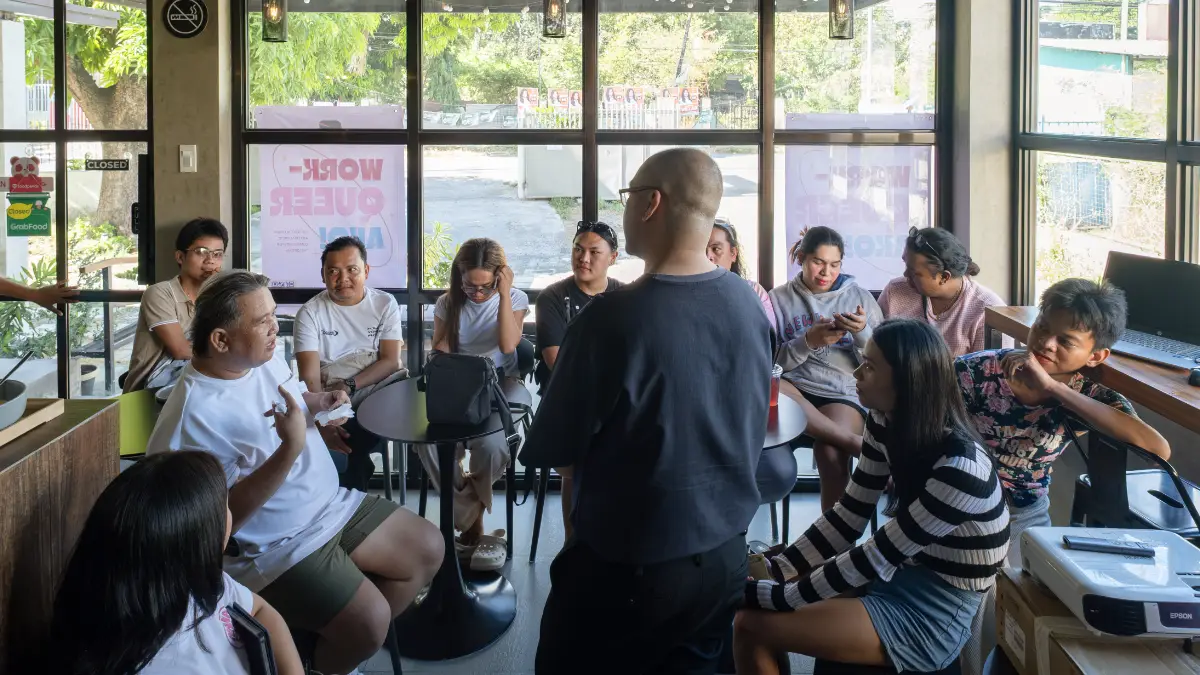 A speaker presenting to a group of people gathered around a small table inside a cafe space.