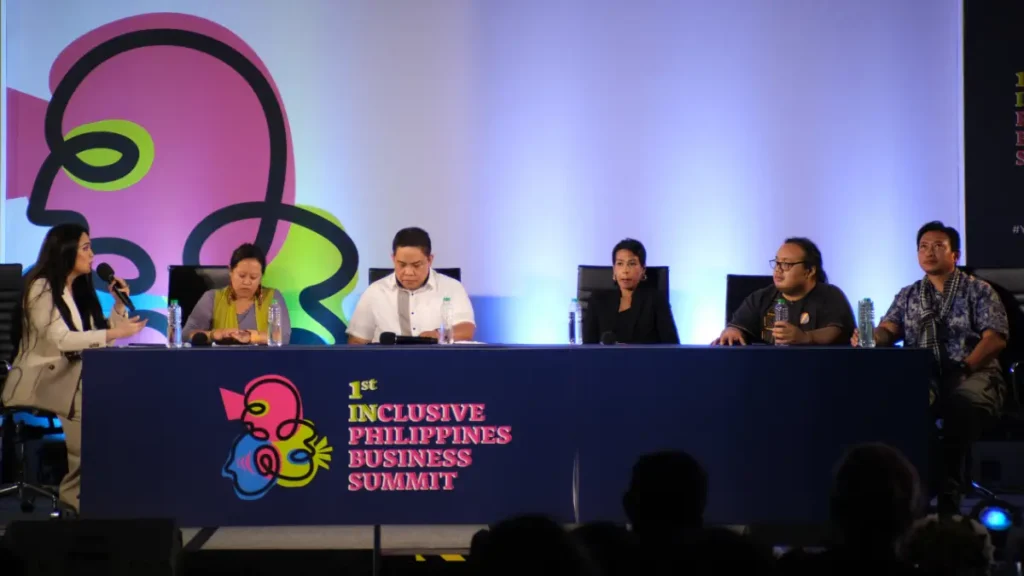 Six panelists sitting at a long table with a microphone setup at the 1st Inclusive Philippines Business Summit.