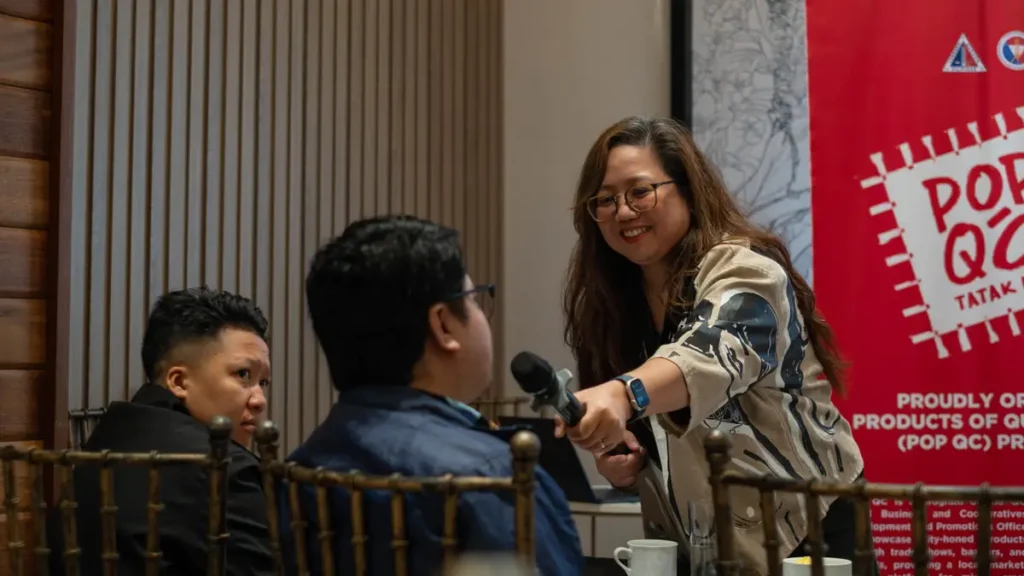 A woman holding a microphone and speaking directly to a man during a workshop session.