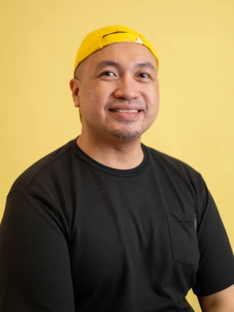 Ronn Astillas, Chair and Executive Director, smiling in a black shirt against a yellow background